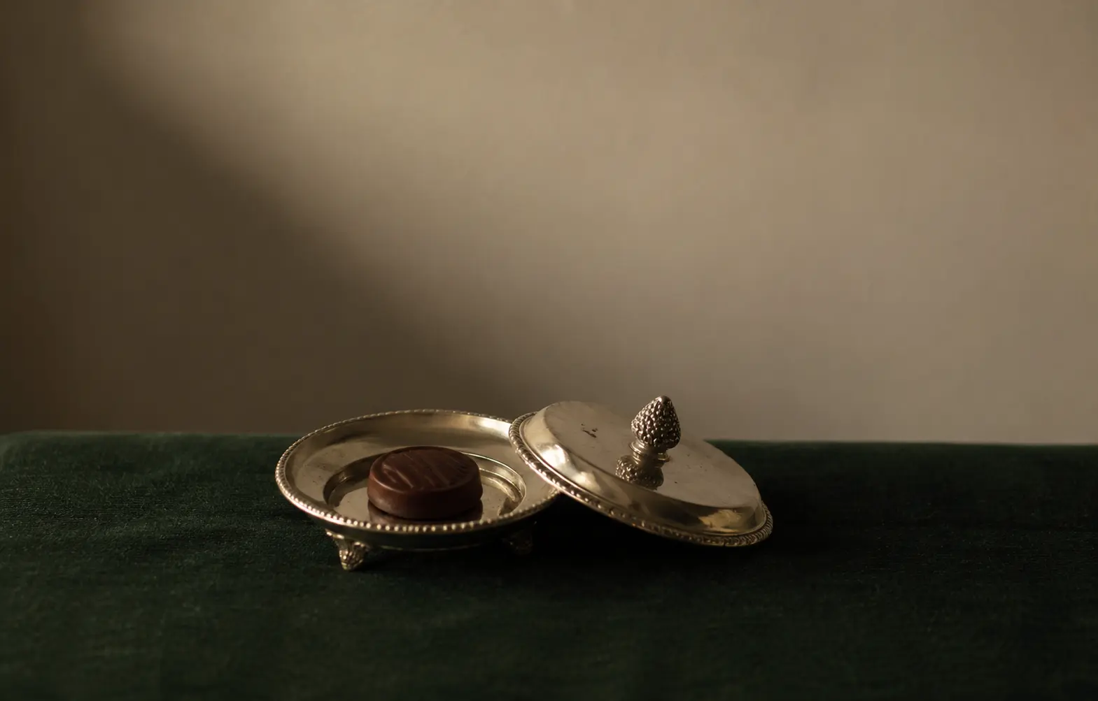A single chocolate mint in an open vintage silver bonbon dish on dark green velvet